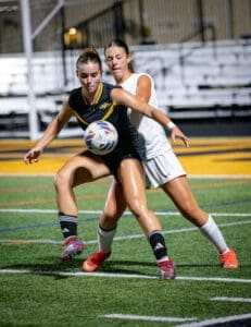 Two female soccer players compete for the ball under stadium lights, showcasing athleticism and competitive spirit.