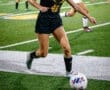 Young female soccer player dribbling a ball on a field during a night match, showcasing athleticism and focus.