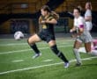 Two female soccer players compete for the ball under stadium lights during a nighttime match on a grassy field.