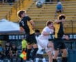Two players jump to head a soccer ball during a match, with spectators in the background. Excitement fills the field.
