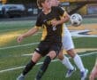 High school soccer players compete for the ball during an evening match on a vibrant turf field.