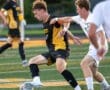 High school soccer players compete for the ball on the field during an intense match, showcasing athleticism and teamwork.