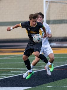 High school soccer players compete for the ball on the field, showcasing athleticism and teamwork during the match.