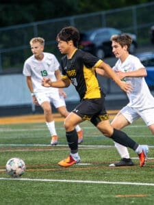 High school soccer match featuring players in action, one sprinting with the ball while opponents chase.