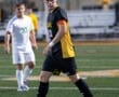 High school soccer players on the field; one in black jersey with C for captain and yellow accents.