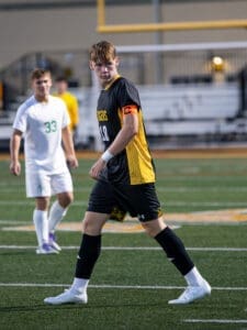 High school soccer players on the field; one in black jersey with C for captain and yellow accents.