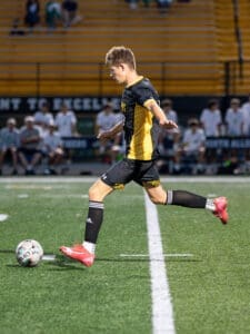Young soccer player in action, kicking a ball on a field with spectators in the background. Energetic game moment.