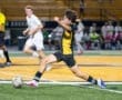 A player in a black and yellow soccer jersey strikes the ball on the field during an intense game night.