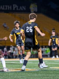 High school soccer players in action, focusing on a player in jersey number 26 dribbling the ball on the field.
