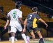 High school soccer players compete on a well-lit field, with player number 7 maneuvering the ball past defender number 3.
