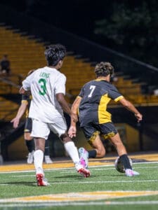 High school soccer players compete on a well-lit field, with player number 7 maneuvering the ball past defender number 3.
