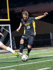 Soccer player in black jersey dribbles a ball on a well-lit field during a nighttime match.