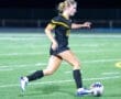 Young female soccer player dribbles a ball on a well-lit field during a night game. Action shot highlighting athleticism.