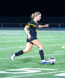 Young female soccer player dribbles a ball on a well-lit field during a night game. Action shot highlighting athleticism.
