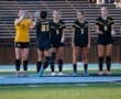 Female soccer players in team uniforms celebrating on the field before a match, showcasing teamwork and sportsmanship.