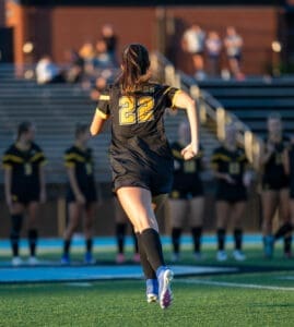 Youth soccer player in black jersey with number 22, running on field with teammates in background during warm-up.