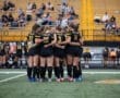 A huddle of female soccer players showing teamwork, unity, and preparation before a match on the field.
