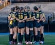 Soccer team huddled together on the field, showcasing unity and teamwork before a match at sunset.