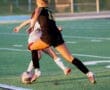 Two female soccer players compete for the ball on a field during sunset, showcasing athleticism and sportsmanship.
