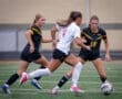 Two soccer players in action on the field, with one dribbling the ball past two opponents in competitive play.