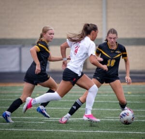 Two soccer players in action on the field, with one dribbling the ball past two opponents in competitive play.