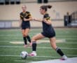 Soccer players on a field; one athlete kicks the ball while the other observes, showcasing team dynamics in action.