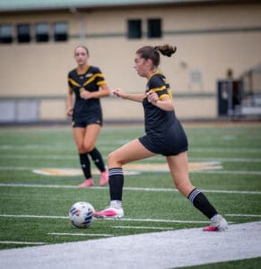 Soccer players on a field; one athlete kicks the ball while the other observes, showcasing team dynamics in action.