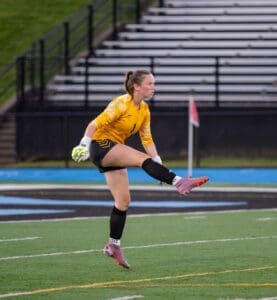 Goalkeeper in a yellow jersey executing a kick on a soccer field, showing agility and focus during the game.