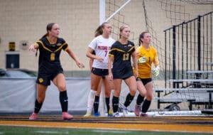Female soccer players on the field, preparing for a play during a competitive match. Goalkeeper in focus.