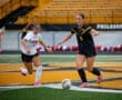 Two female soccer players compete for the ball on a vibrant field during a game, showcasing athleticism and teamwork.