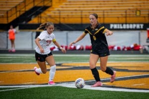 Two female soccer players compete for the ball on a vibrant field during a game, showcasing athleticism and teamwork.