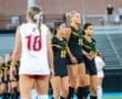 Three female soccer players in black uniforms line up on the field, focused and ready for the upcoming play.
