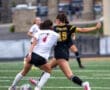 Two female soccer players compete for control of the ball during an intense match on a green turf field.