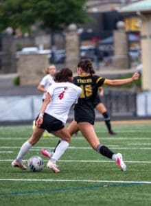 Two female soccer players compete for control of the ball during an intense match on a green turf field.