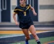Young female soccer player in a black and yellow jersey dribbling a soccer ball on the field, focused on the game.