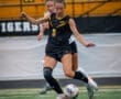 Two female soccer players compete for the ball on a turf field, showcasing athleticism and teamwork.