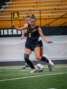 Two female soccer players compete for the ball on a turf field, showcasing athleticism and teamwork.