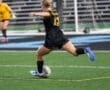 Female soccer player in black jersey dribbles a ball on the field during a match, showcasing skill and athleticism.