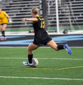 Female soccer player in black jersey dribbles a ball on the field during a match, showcasing skill and athleticism.