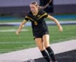 Female soccer player in a black jersey dribbling a ball on a field during a match, showcasing athletic skill and focus.