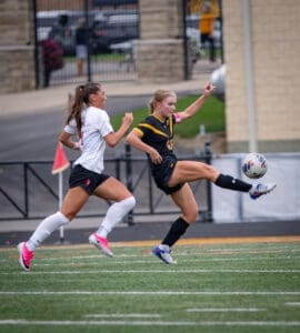 Two female soccer players compete for the ball on the field, showcasing athleticism and teamwork in action.