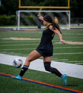 A soccer player in black uniform kicks a ball on the field during a game, showcasing athletic movement and skill.