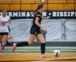 Player in black jersey dribbles soccer ball on field, with teammate in white jersey nearby. Game action captured clearly.