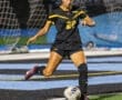 Soccer player in black uniform kicking a ball on the field during a night game. Focus on athletic action and teamwork.