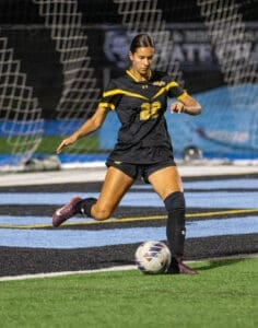 Soccer player in black uniform kicking a ball on the field during a night game. Focus on athletic action and teamwork.