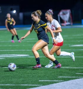 Two female soccer players compete for the ball on an illuminated field during a night game. Exciting athletic action captured.