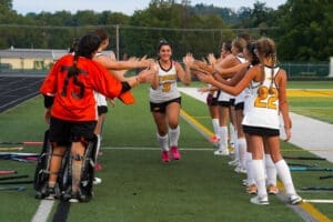 High school field hockey players celebrate with a teammate during a game, creating a spirited and enthusiastic atmosphere.
