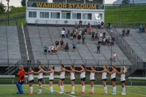 Field hockey players and fans gather at Warrior Stadium for an evening match, showcasing school spirit and community support.