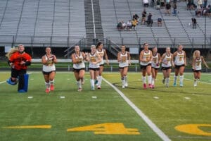 Field hockey team running on the field after a game, showcasing teamwork and excitement in sports attire.