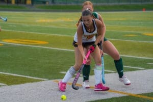 Two field hockey players compete for the ball on a turf field, showcasing dynamic athleticism and teamwork.